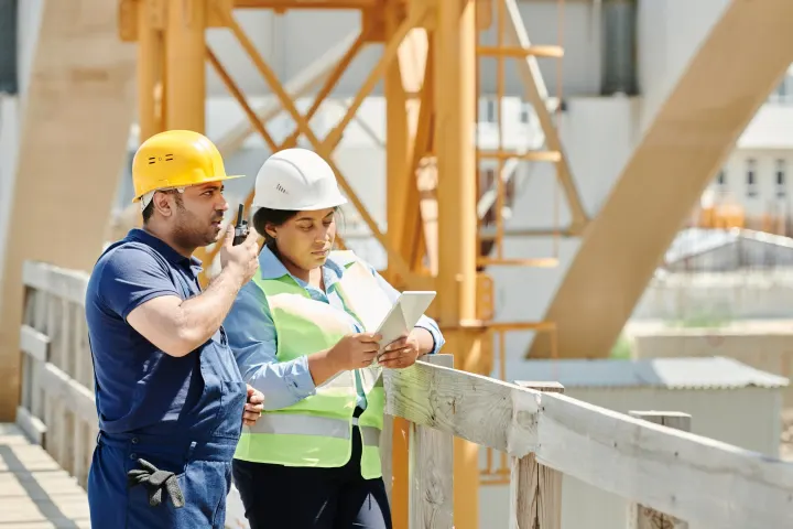 A construction professional uses a tablet beside an active job site.